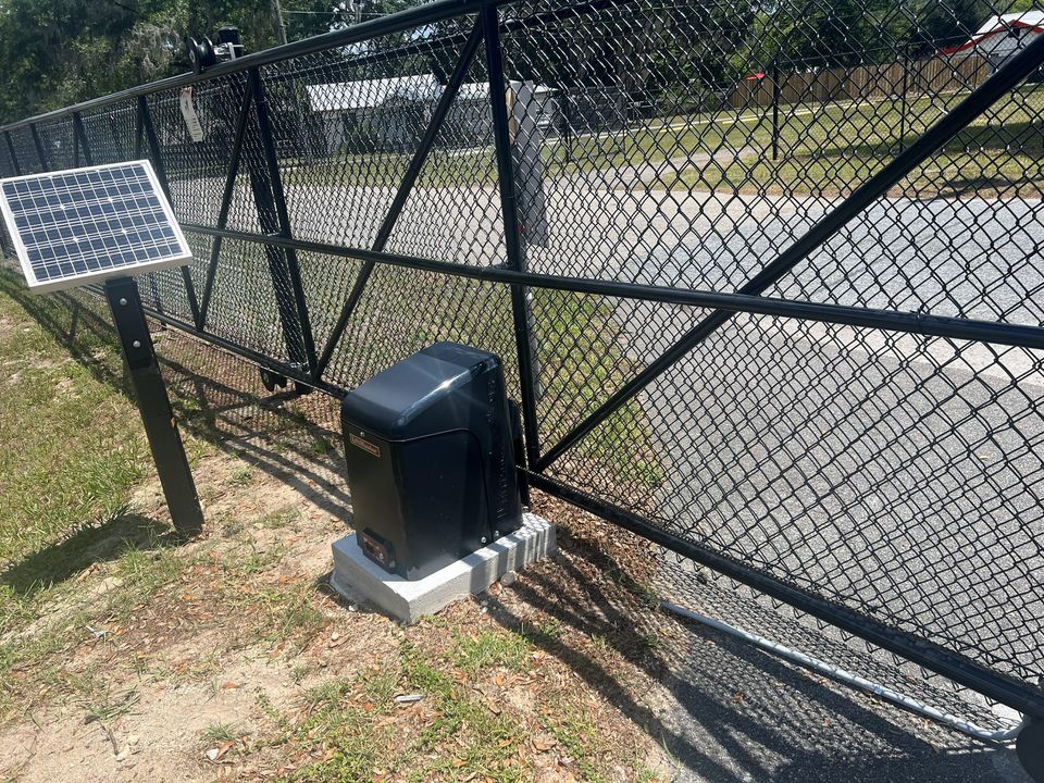 Solar-powered gate operator mounted on a black chain-link swing gate.