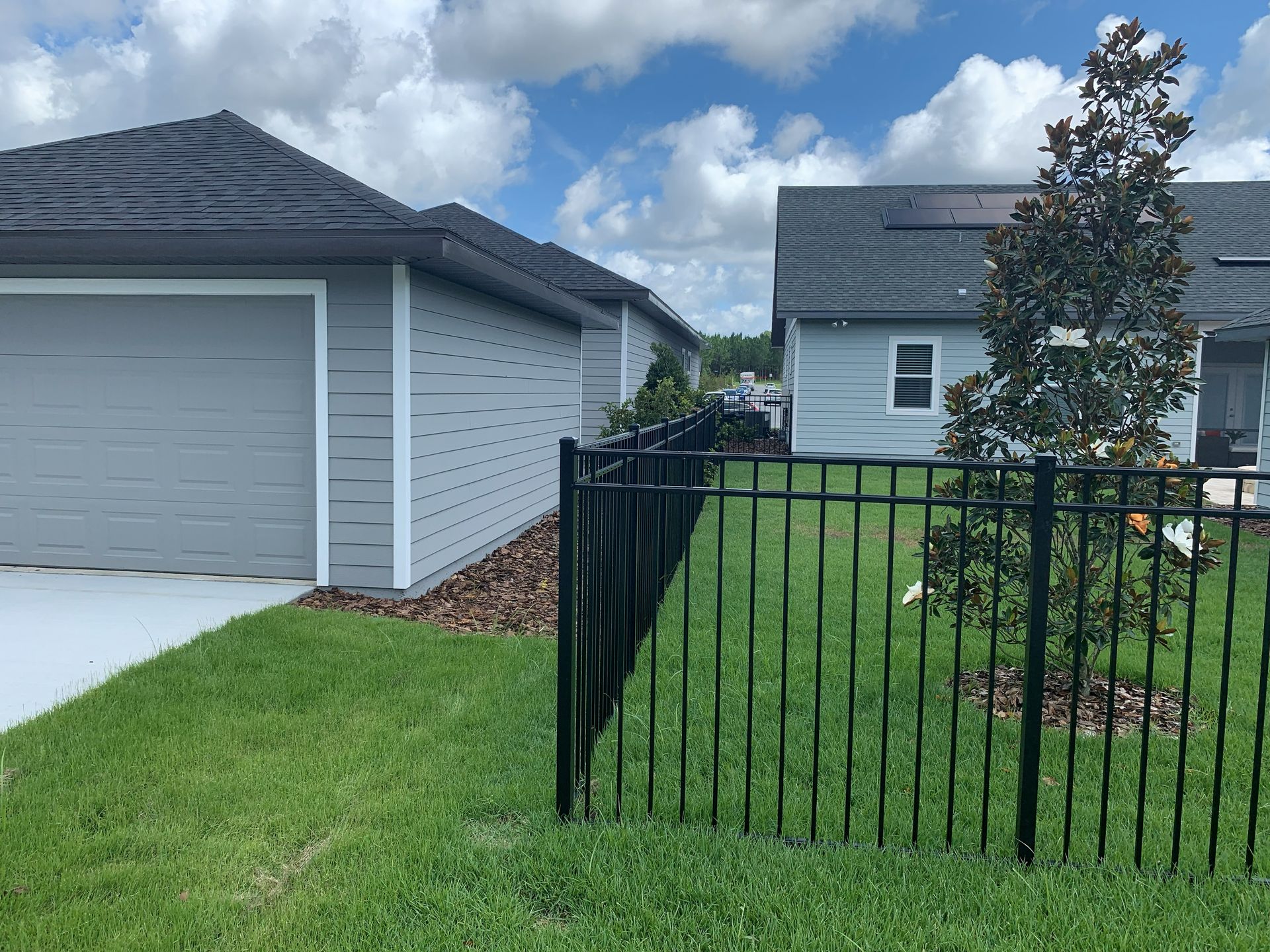 Black aluminum picket fence bordering a landscaped side yard between two houses.