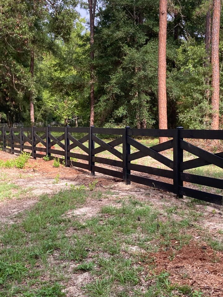 Black four-rail ranch-style wood fence along a wooded acreage lot.