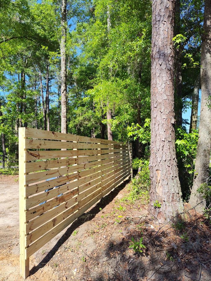 Freshly built horizontal-slat wood privacy fence along a wooded property line.