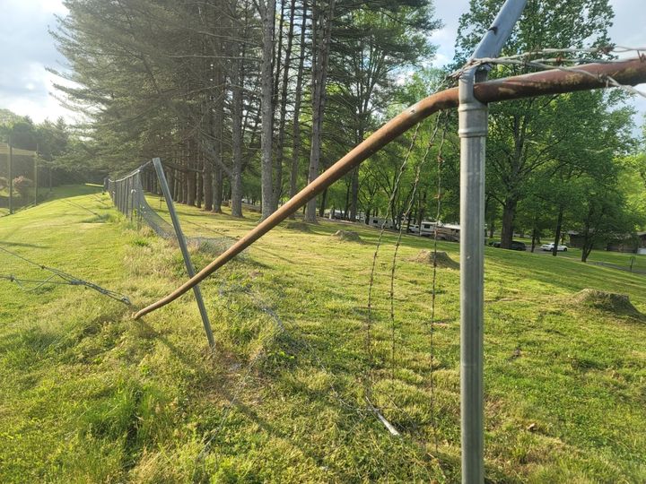 Badly bent chain-link top rail and post along a long damaged fence run.