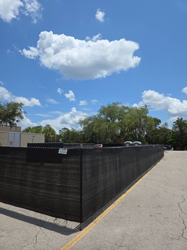 Temporary fence panels with black privacy screening around a paved work area.