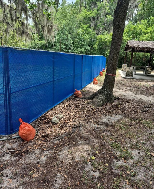 Blue privacy windscreen on a temporary chain-link fence, held down with ballast weights.