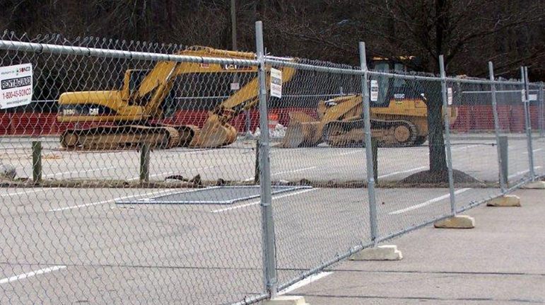 Temporary chain-link fence enclosing construction equipment, including excavators, at a job site.