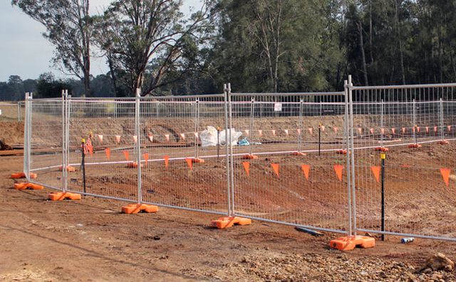 Freestanding temporary chain-link fence panels on orange stabilizer feet at a construction site.