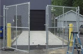 Temporary chain-link swing gate with yellow bollards at a commercial loading area.